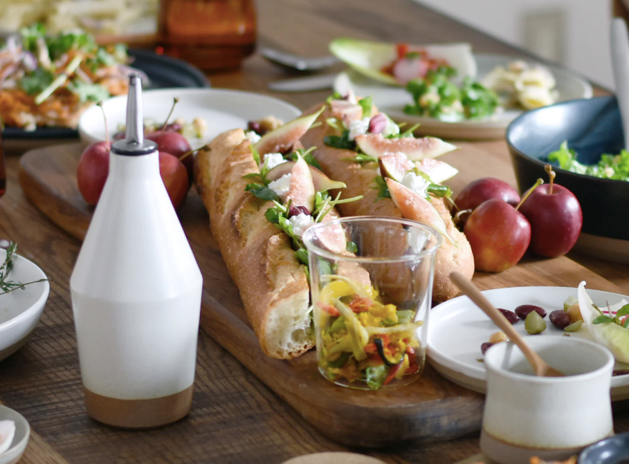 Wooden table with a sandwich, salad, and various condiments on a rustic setting